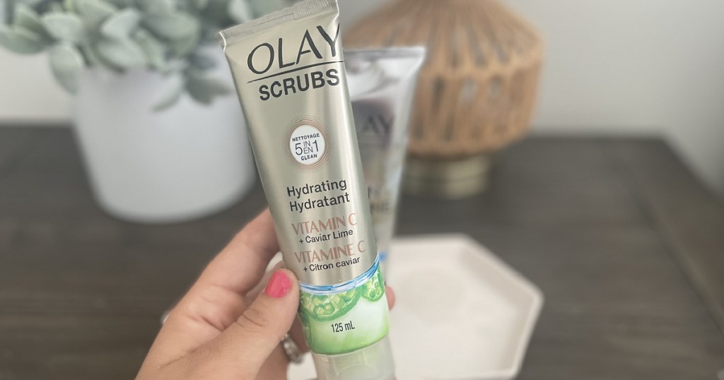 hand holding olay scrub in front of artificial plant