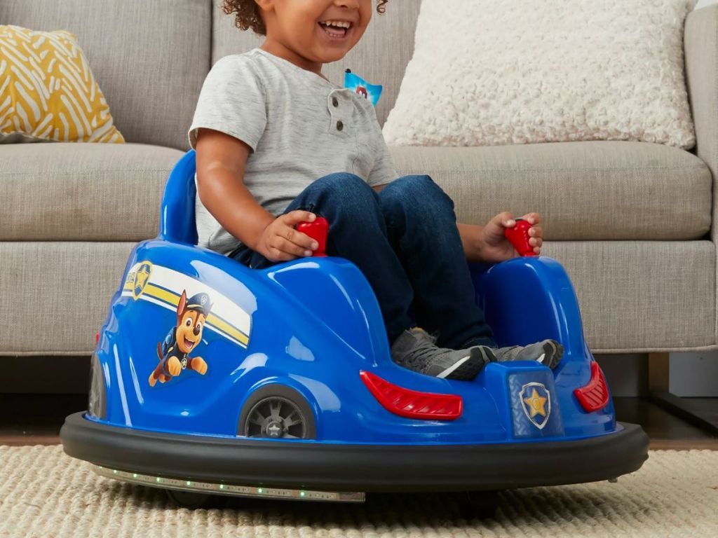 a little boy riding a PAW Patrol 6V Bumper Car in a living room