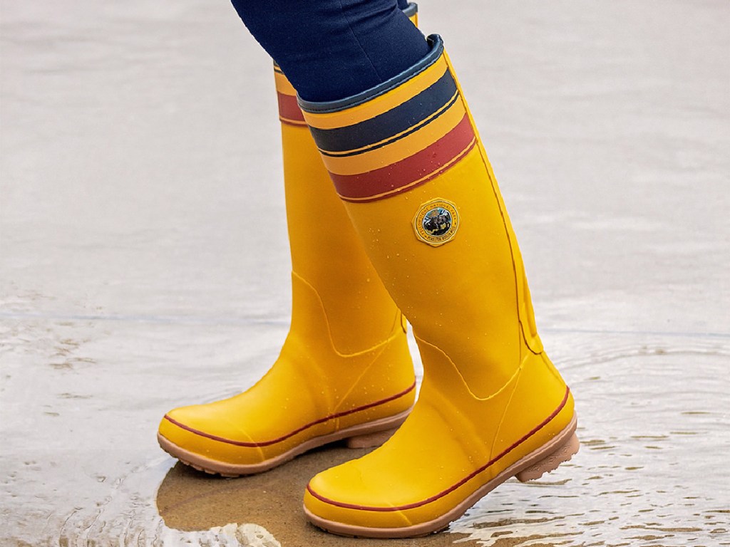 woman wearing pair of tall yellow rain boots in puddle