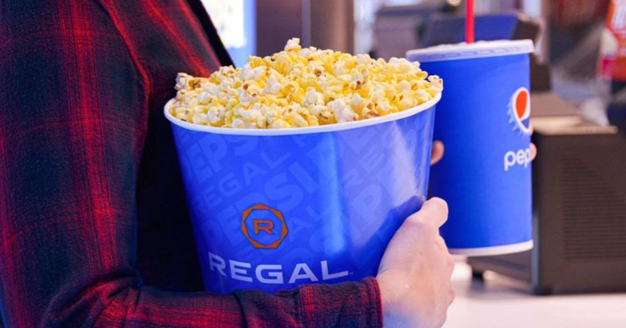 Hands holding a huge bucket of popcorn and a fountain soda from Regal Cinemas