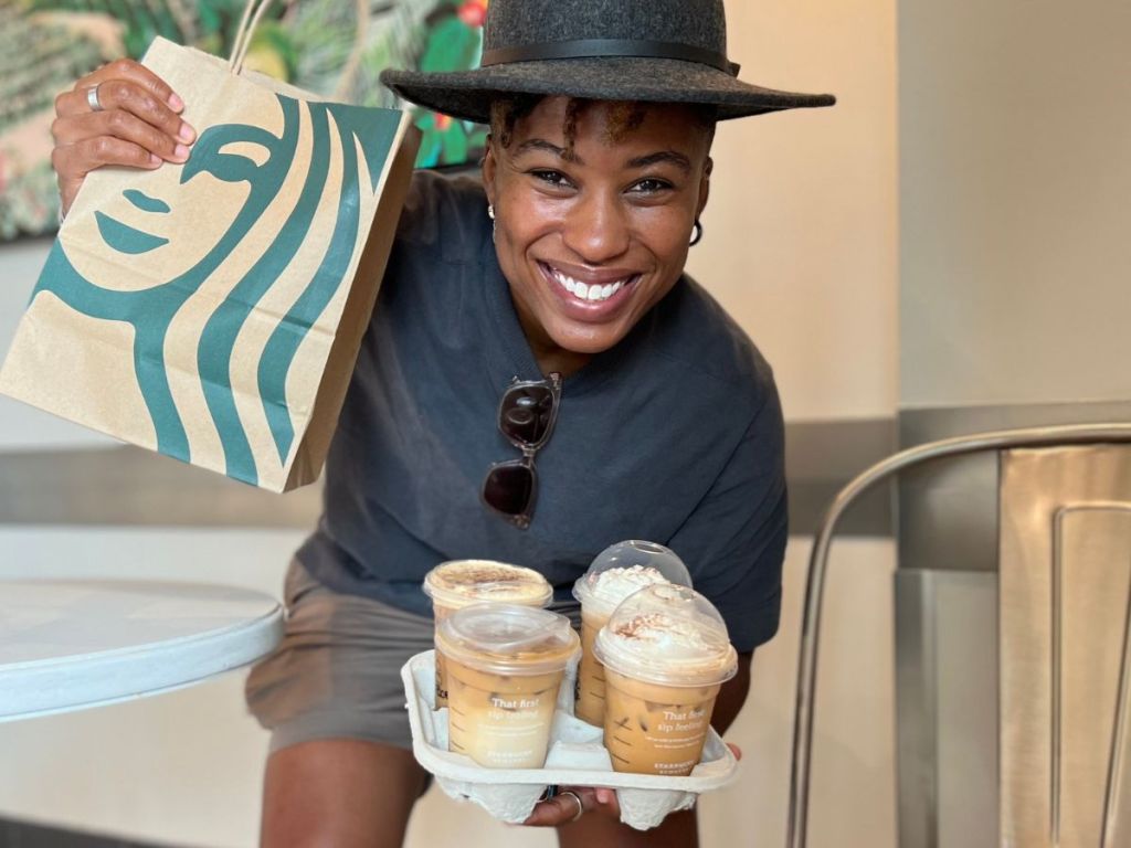 Woman holding a tray of four Starbucks drinks and a Starbucks bag