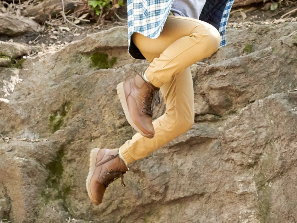 boy jumping by rocks wearing brown boots