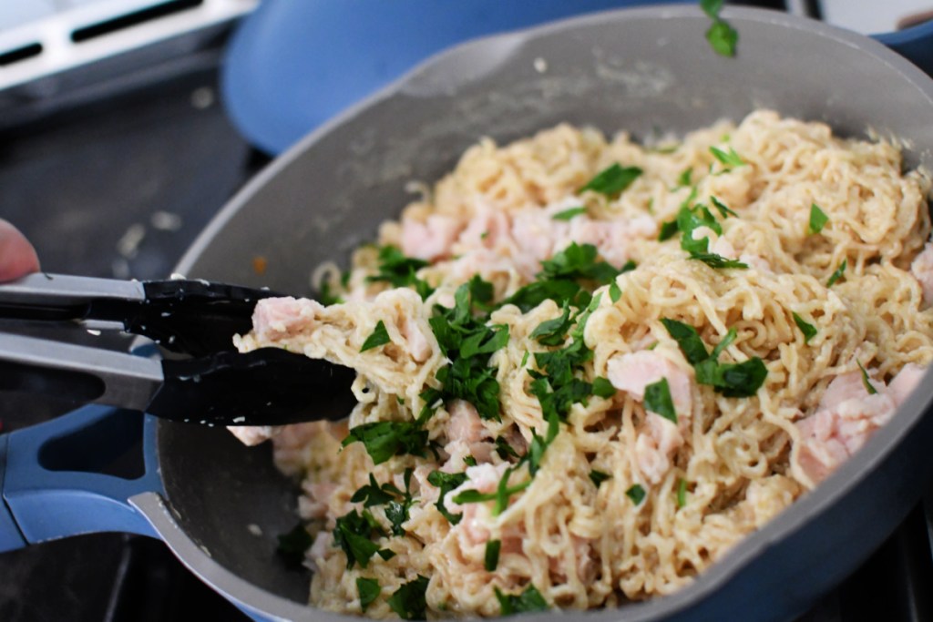 adding canned chicken and fresh parsely to pan of ramen alfredo
