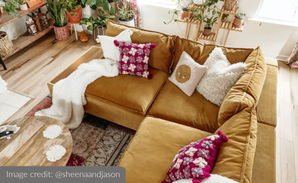 gold velvet sectional in boho living room with colorful pillows and green plants