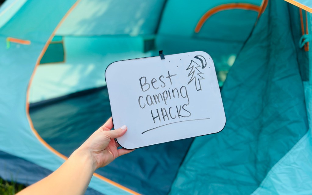 hand holding a dry erase board with best camping hacks written on front