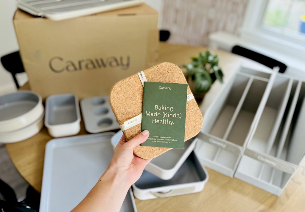 hand holding caraway bakeware pamphlet and cork hot pads