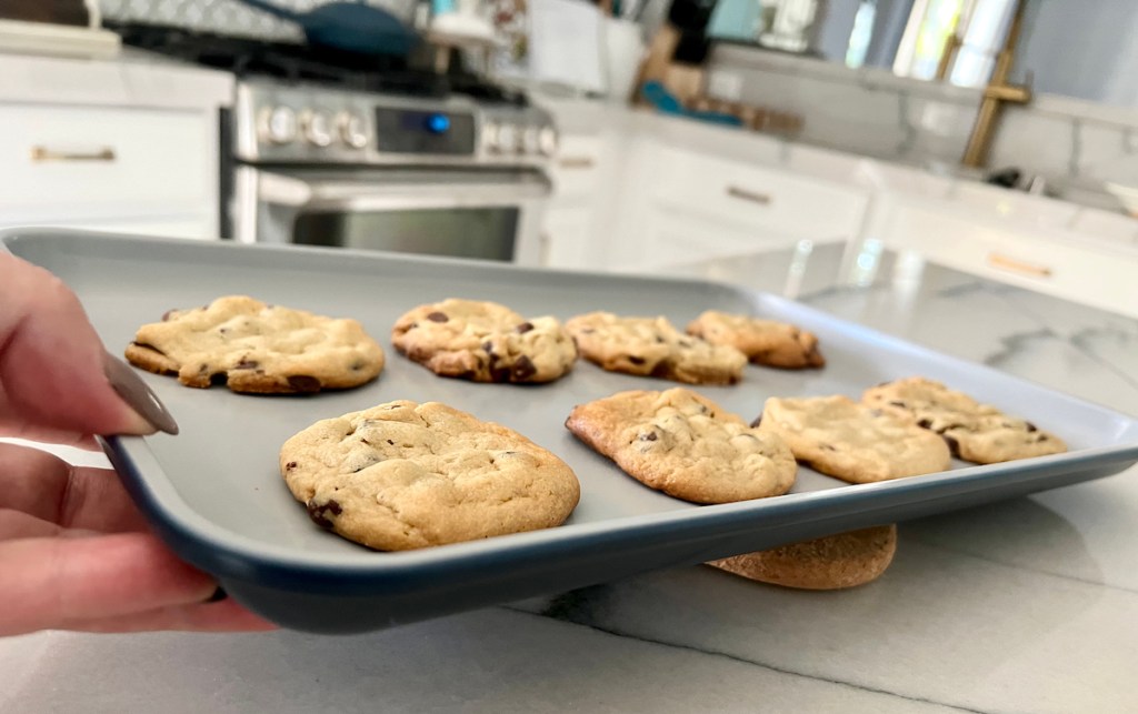 hand holding a blue sheet pan with chocolate chip cookies on top