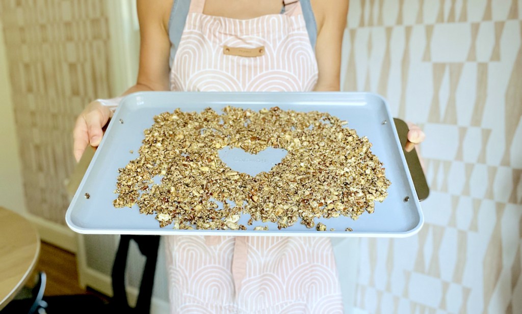 woman holding sheet pan with granola and heart in middle