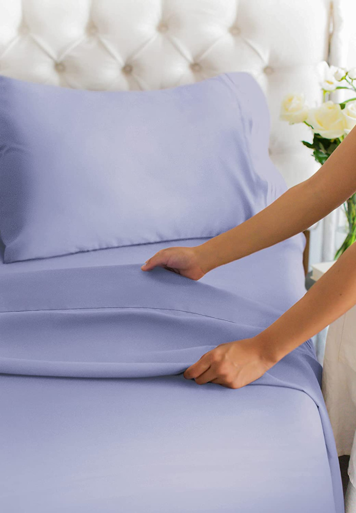 woman making a white tufted headboard bed with light purple blue cgk sheets