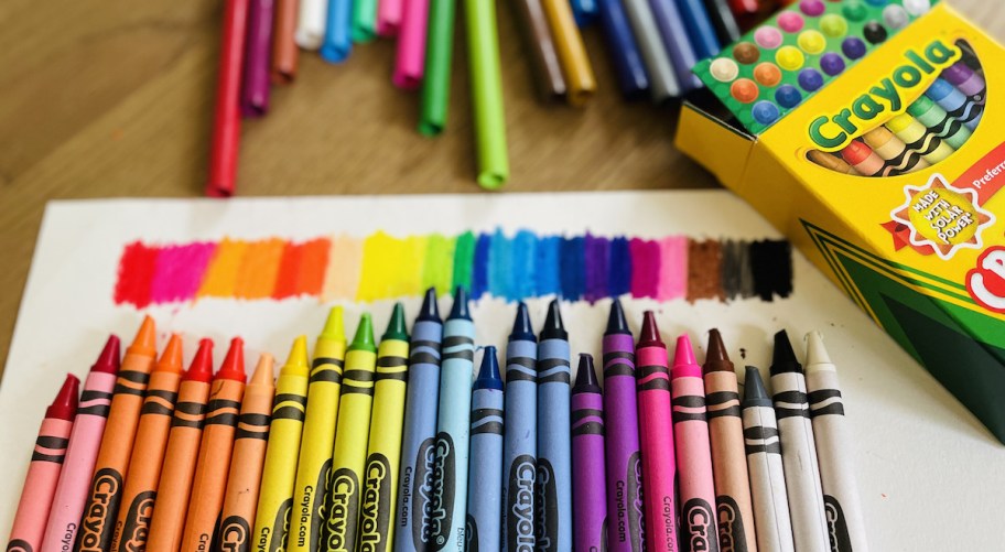 rainbow row of crayons on table with white paper and testing colors