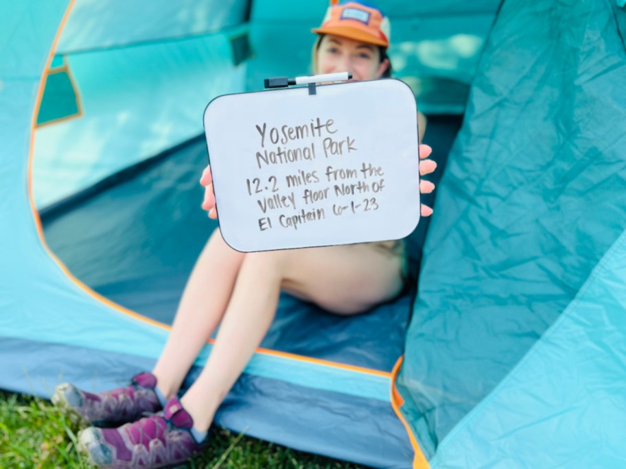 woman holding dry erase board in tent with camping ideas information
