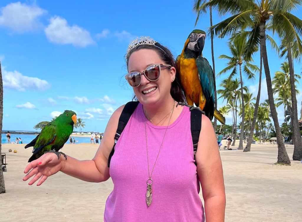 woman holding parrots on beach outside wearing tiara