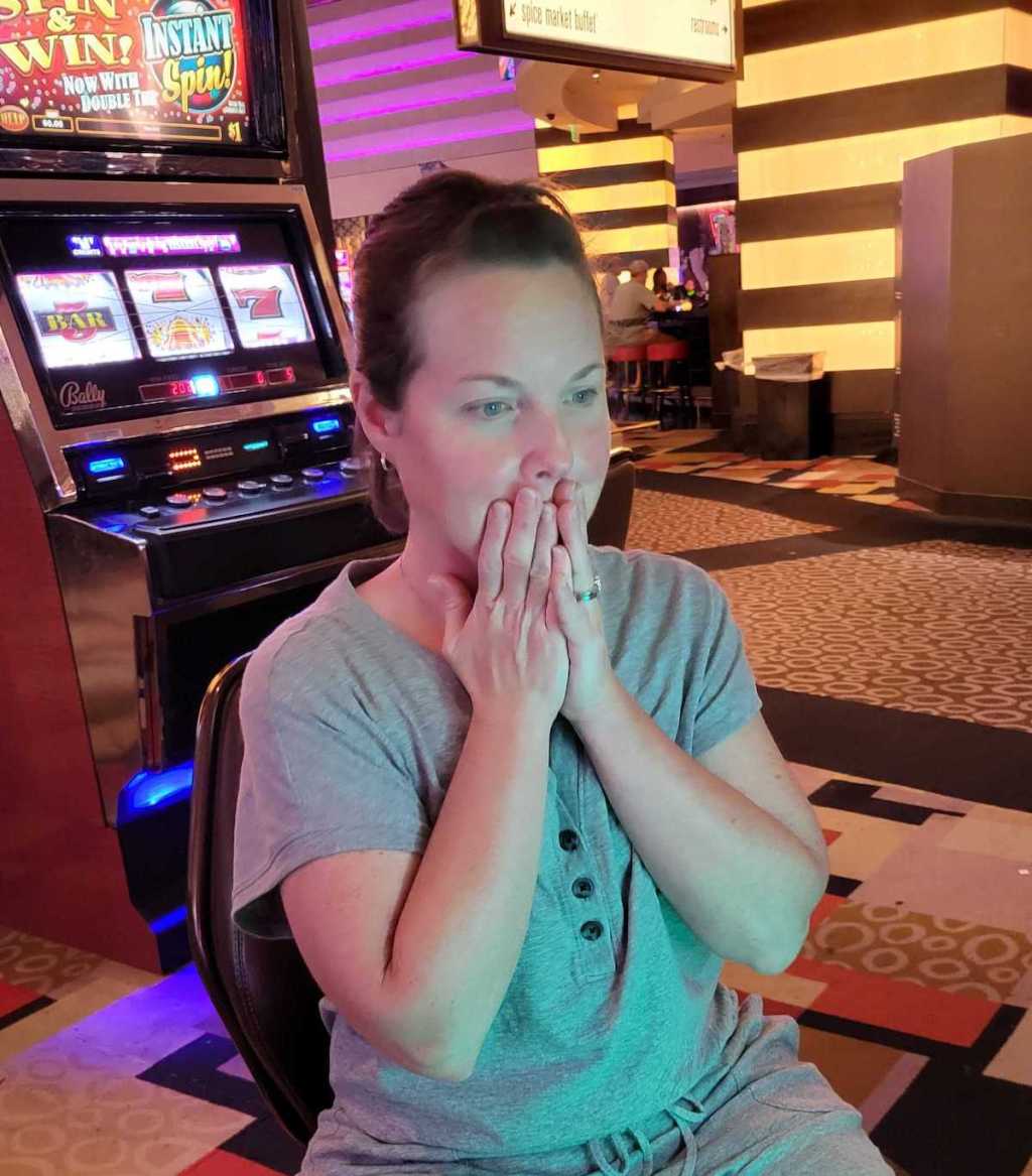 woman with hands over mouth sitting at slot machine in las vegas