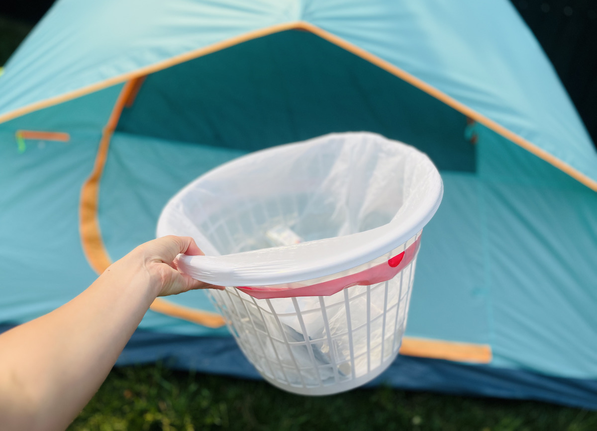 hand holding a laundry basket with trash bag inside in front of tent for camping ideas