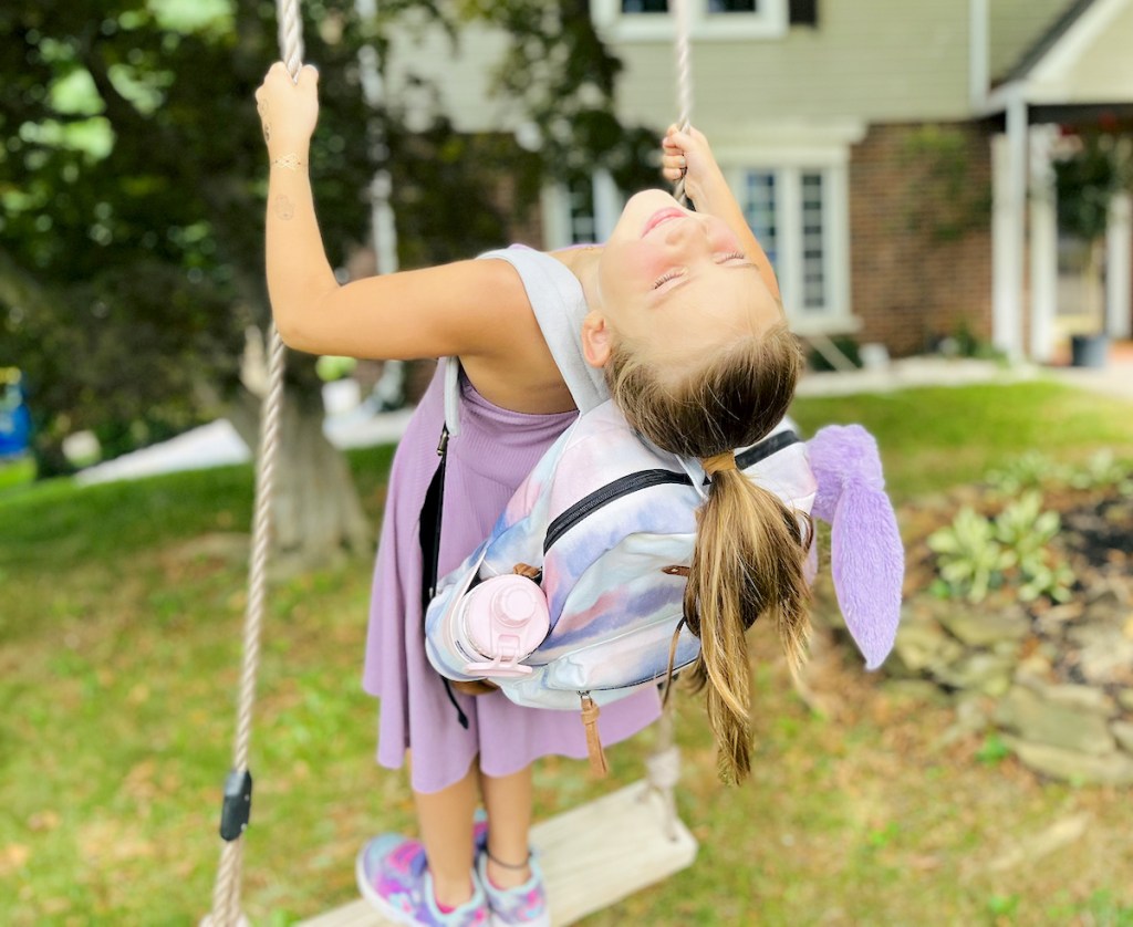 girl swinging on outdoor tree swing with bookbag