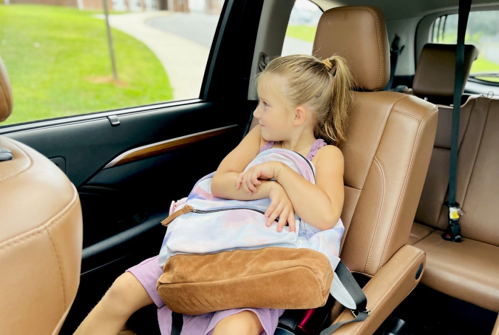girl sitting in car hugging tie dye bookbag