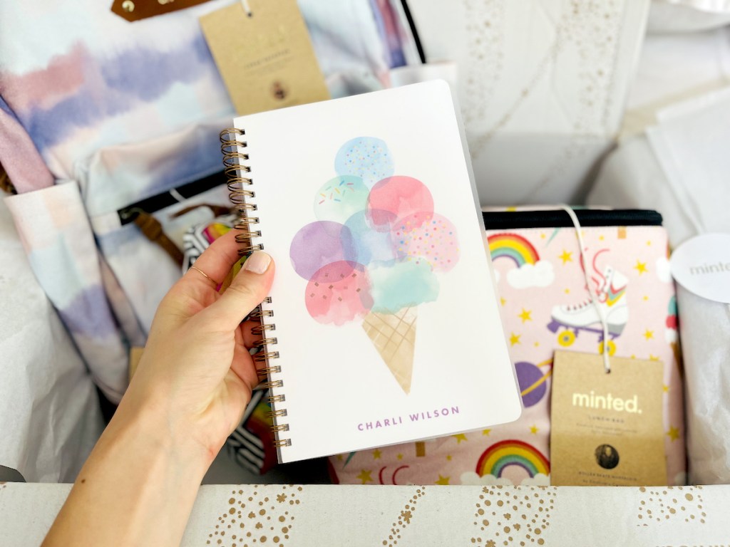 hand holding ice cream notebook over box of back to school stuff