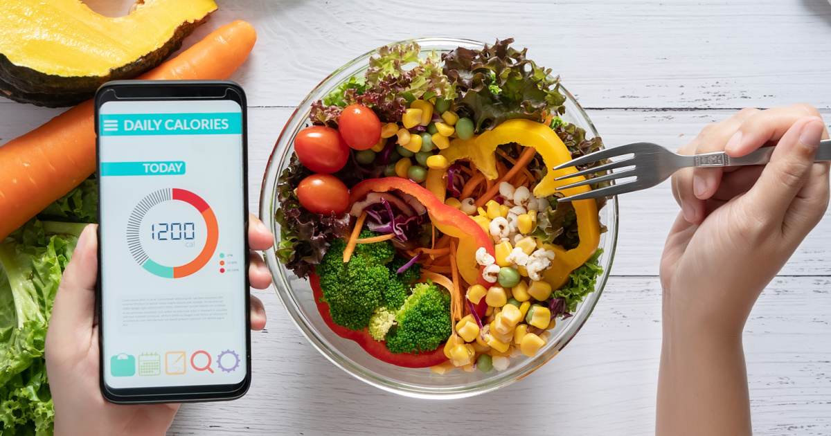 person holding a smart phone and a fork over a bowl of salad