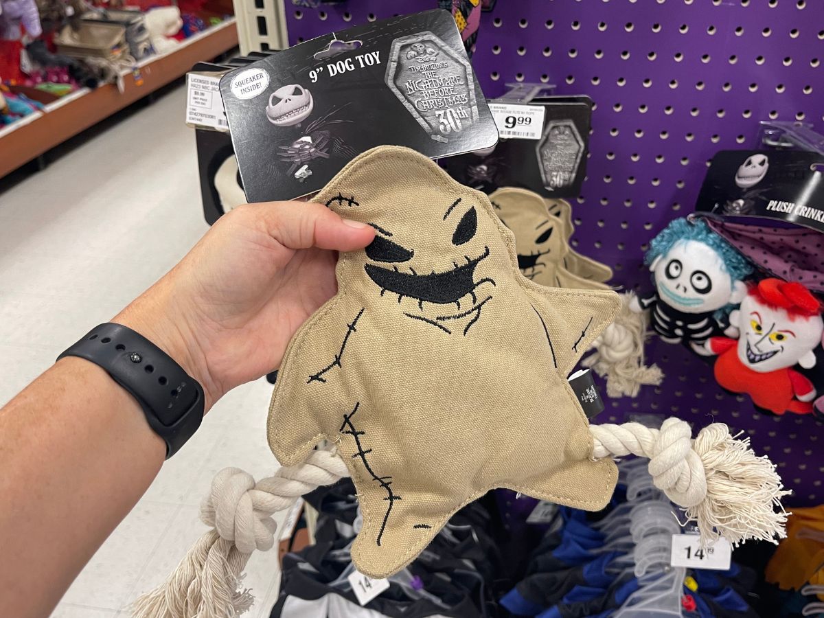a womans hand holding an oogie boogie dog toy