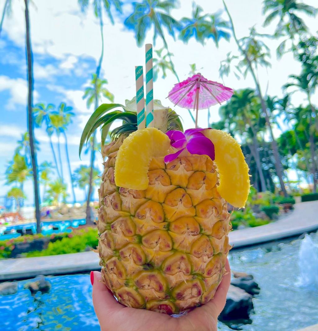 hand holding a summer pineapple drink in front of ocean