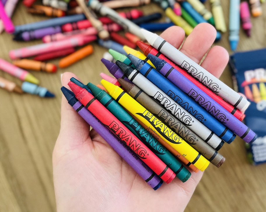 hand holding tons of different colors of prang over table with lots of colorful wax