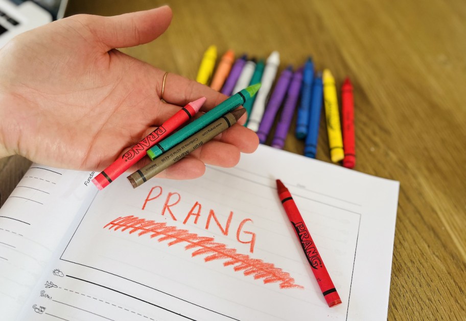 hand holding crayons over paper with prang written on top