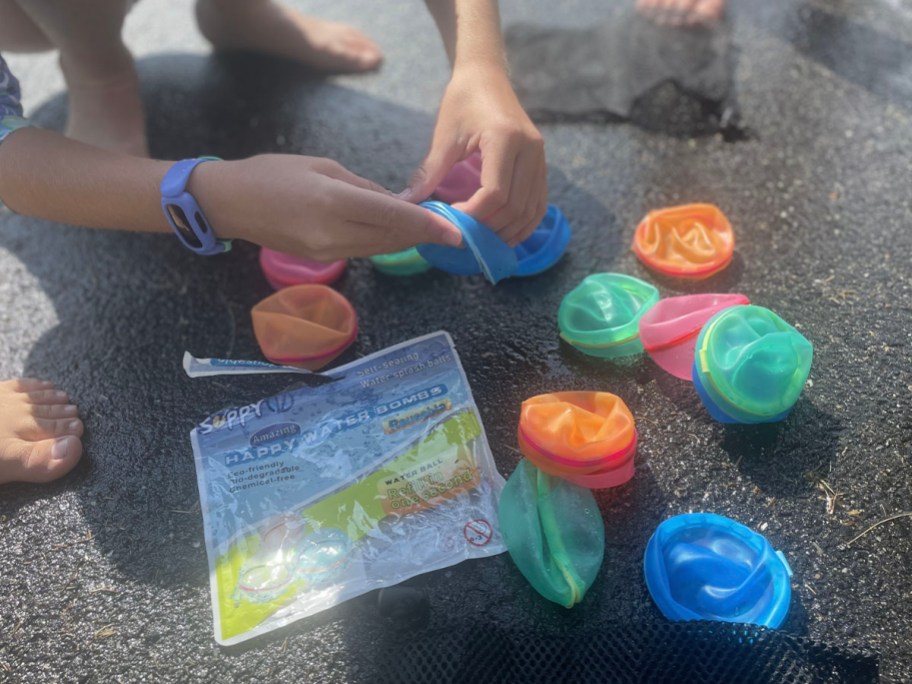 pack of water balloons laying on ground with child opening one