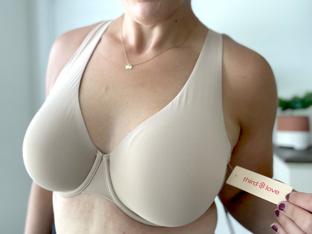 close up of woman wearing nude bra holding thirdlove bra tag