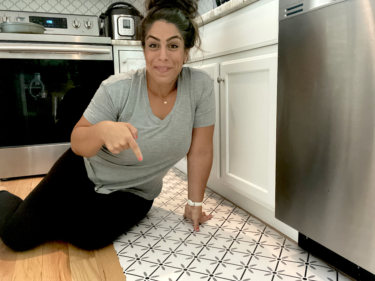 woman sitting on kitchen floor pointing to vinyl floor mat