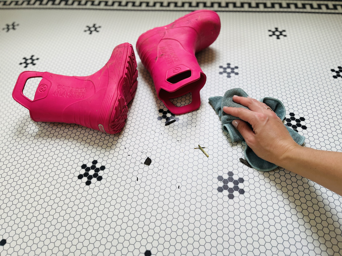 pink rain boots laying on floor with hand cleaning up dirt on floor
