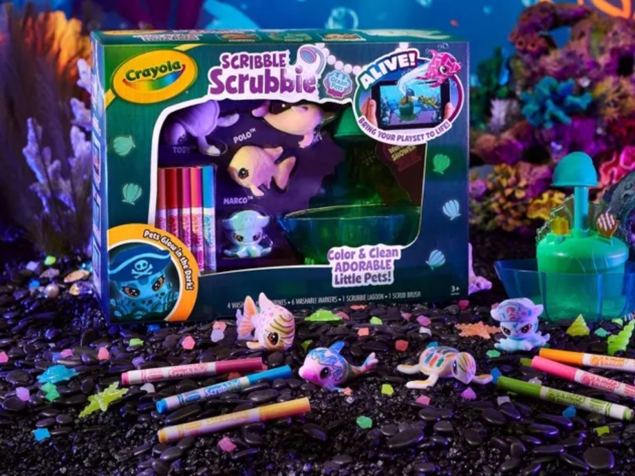 a Crayola Scribble Scrubble Lagoon activity set in the box, and markers and toys in front of it on a dark ocean background