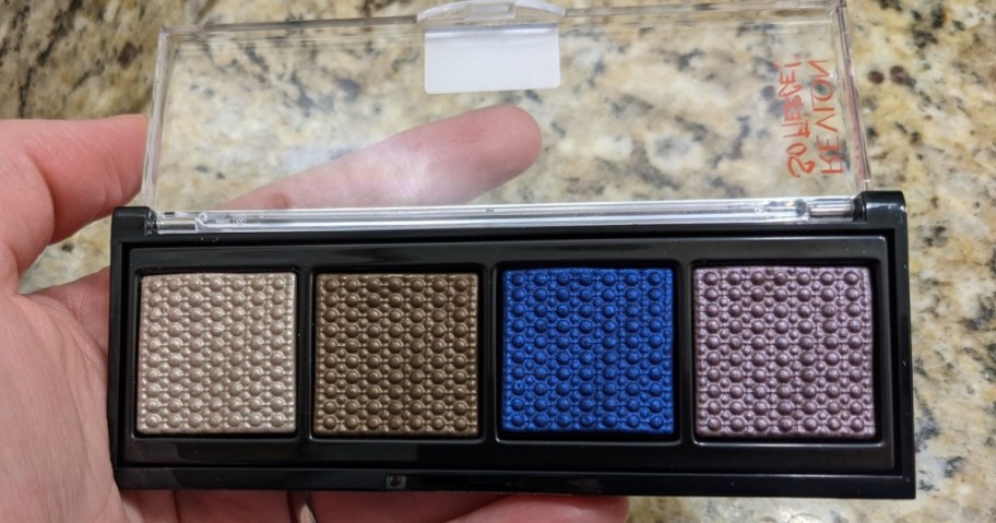 hand holding an open Revlon eyeshadow palette with 4 colors, bathroom counter behind it