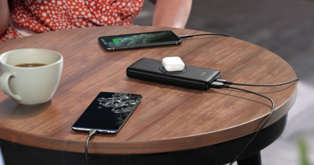 Anker 533 Wireless Power Bank charging earbuds, and two phones on a table