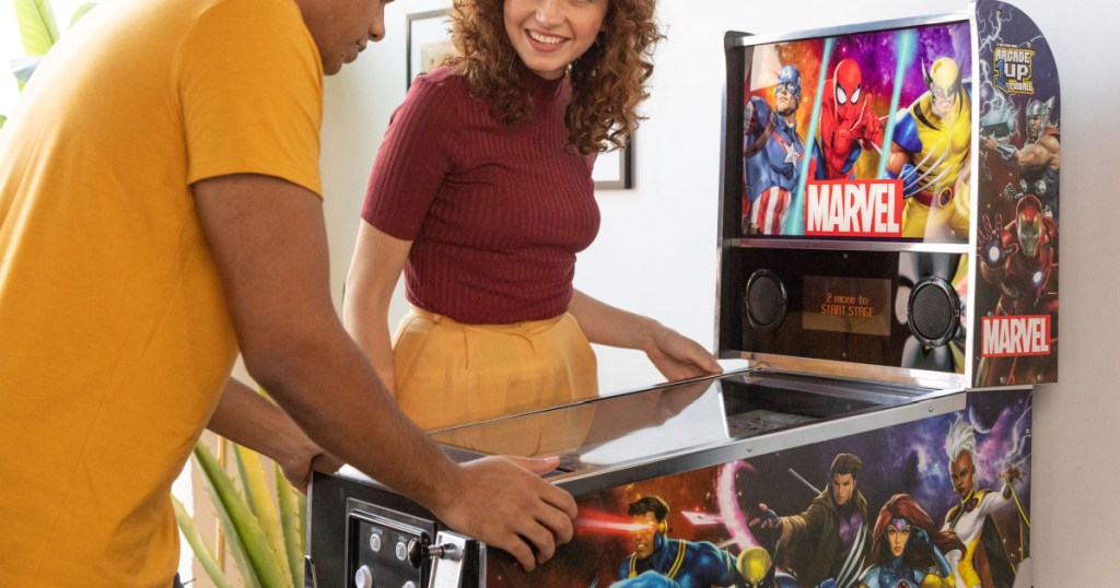 man and woman playing with Marvel pinball machine