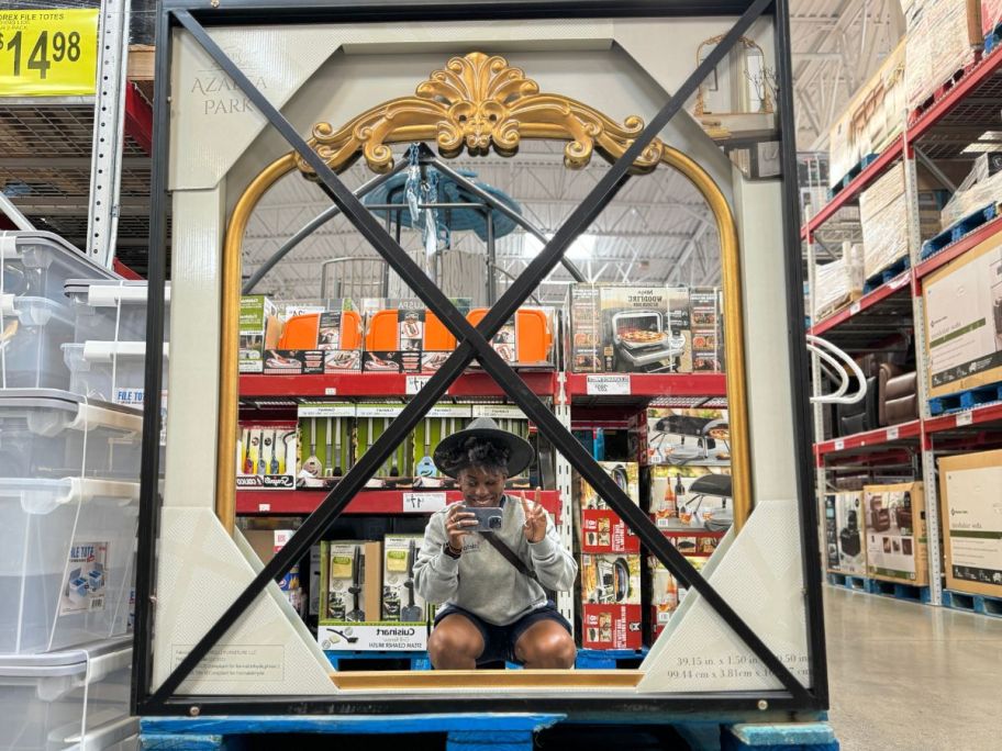 A woman taking a picture of an Azalea Park Filigree Mirror in Sam's Club