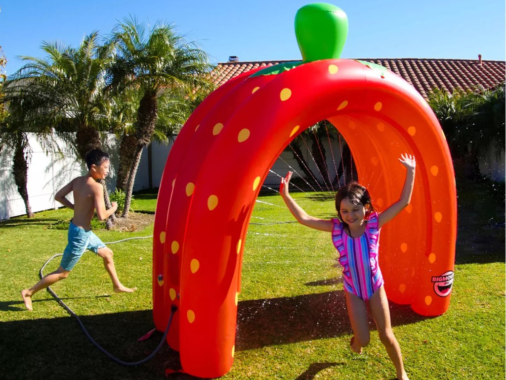 kids running through inflatable strawberry sprinkler in yard