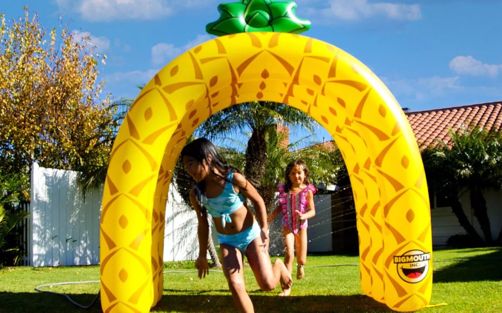 kids running through inflatable pineapple sprinkler in yard