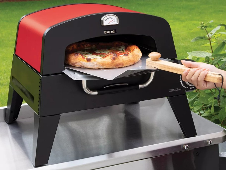 person putting a pizza in a red and black outdoor pizza oven