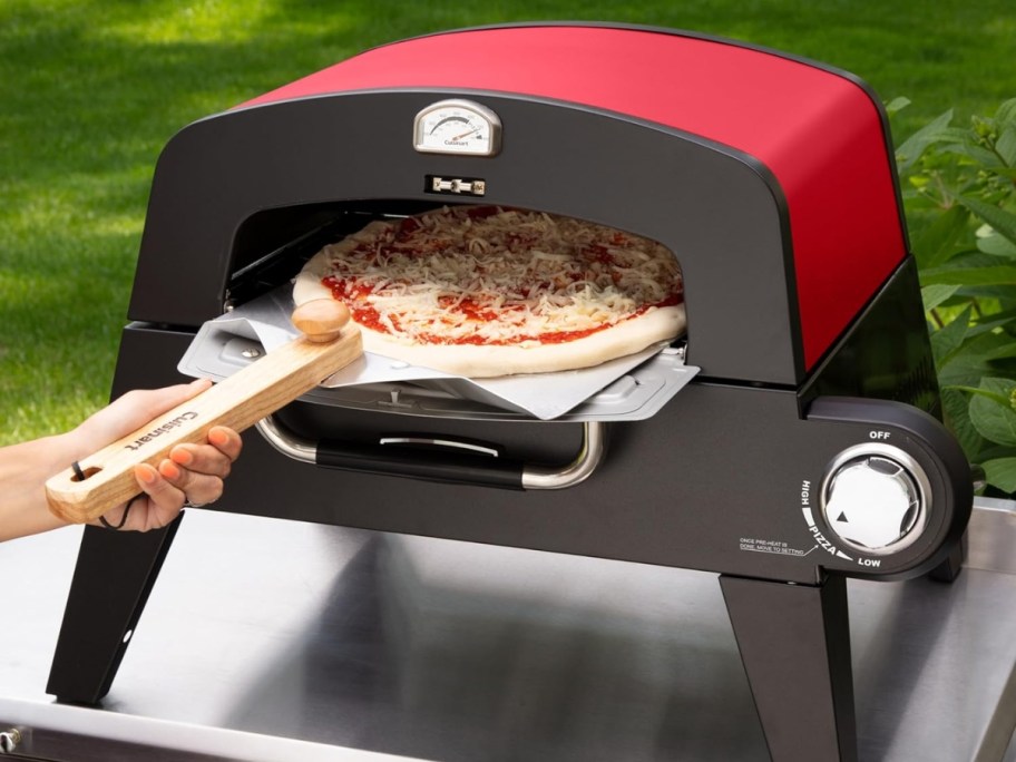 person putting a pizza in a red and black outdoor pizza oven