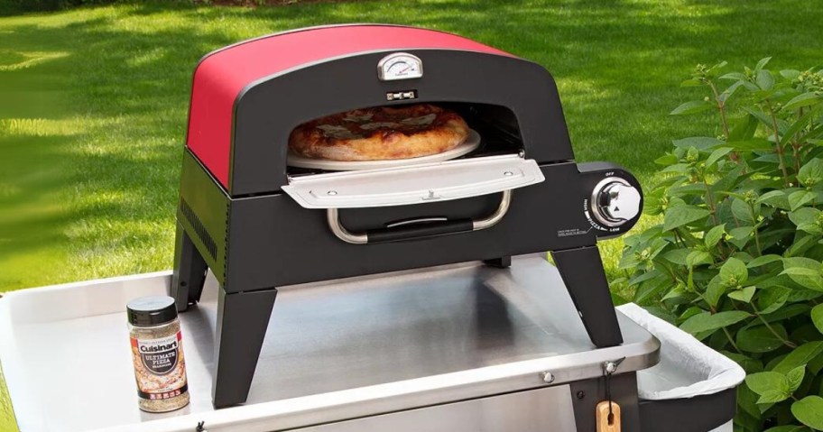 red and black outdoor pizza oven on a silver table, open showing pizza inside