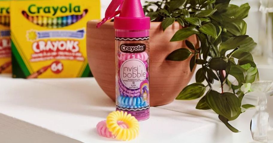 invisibobble Multipack Hair Elastics - Crayola - 10ct in crayon shaped container on shelf with plant and box of Crayola crayons behind it