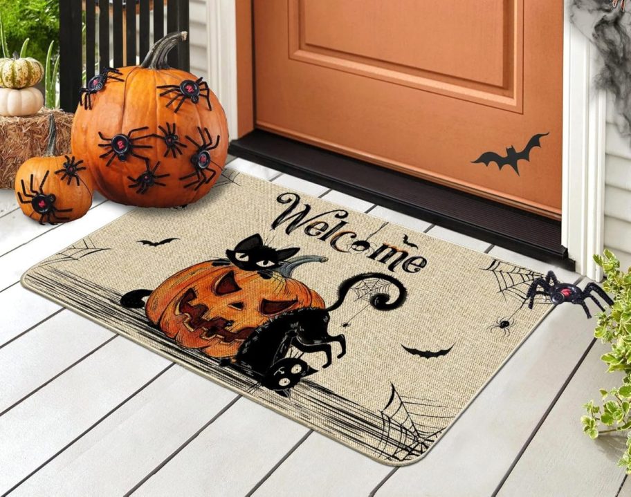 A Halloween doormat with a pumpkin jack o lantern and black cats, bats, and spiders