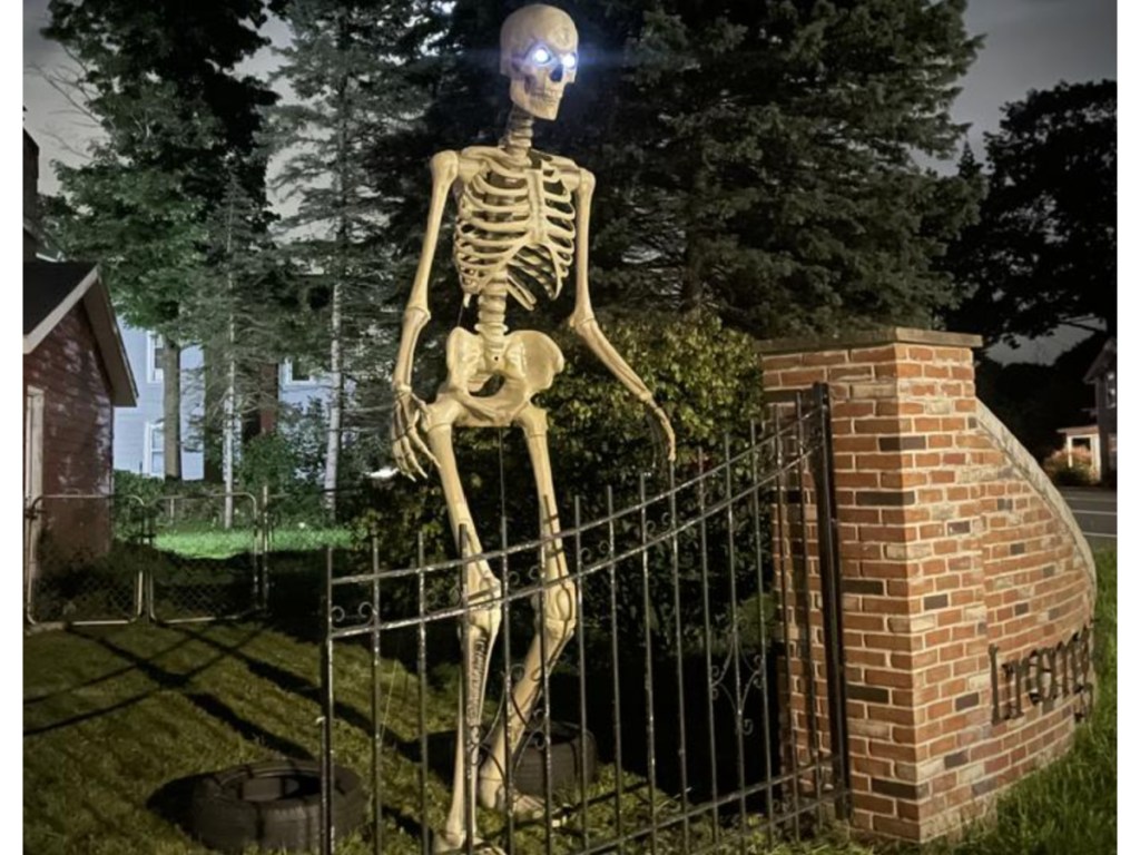 super tall skeleton on display in yard in front of gate