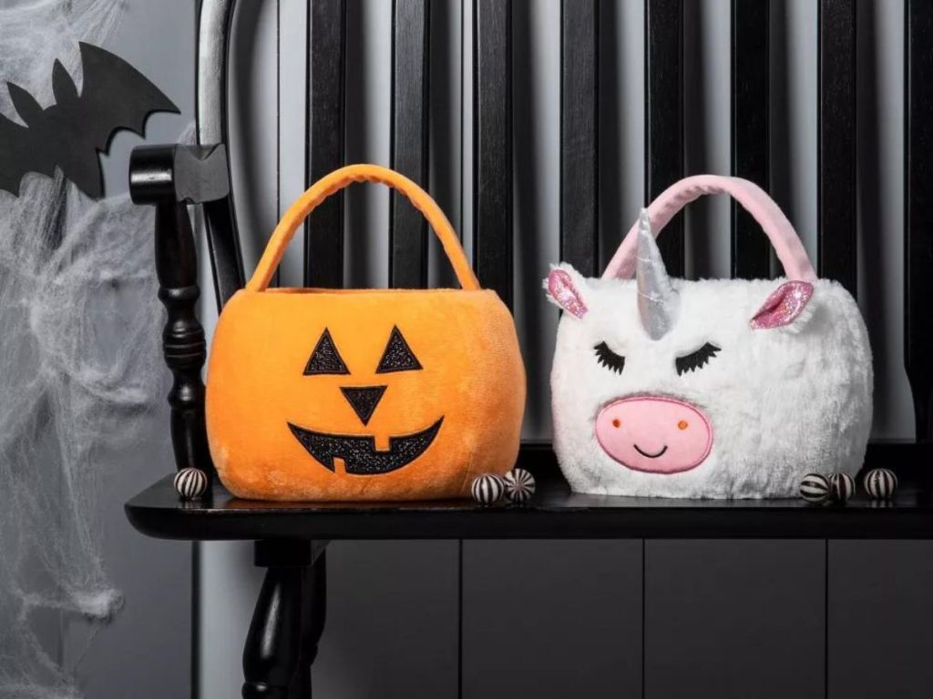 Plush Trick or Treat pumpkin and unicorn pail on black bench