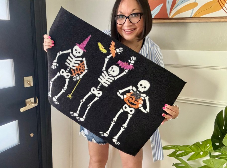 Woman holding up a Halloween Doormat with skeletons on it