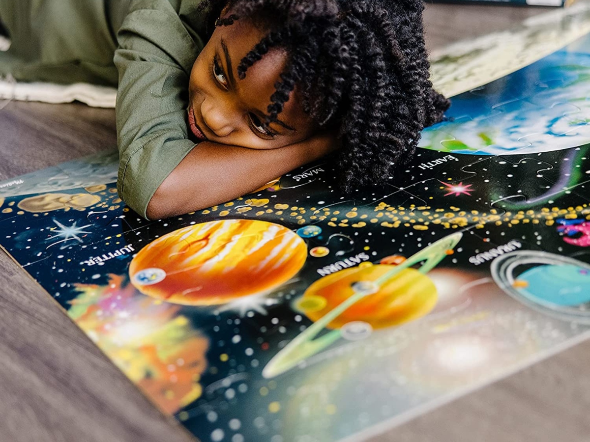 child laying on floor, with completed solar system floor puzzle