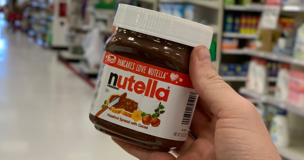 A hand holding a jar of Nutella in a store.