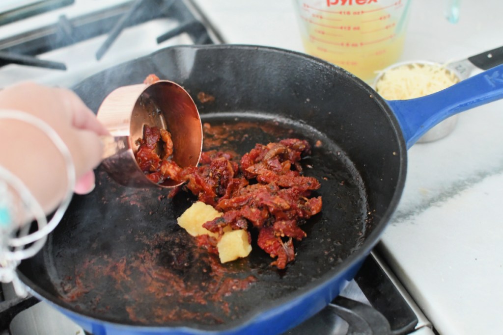 adding garlic and sundried tomatoes to skillet