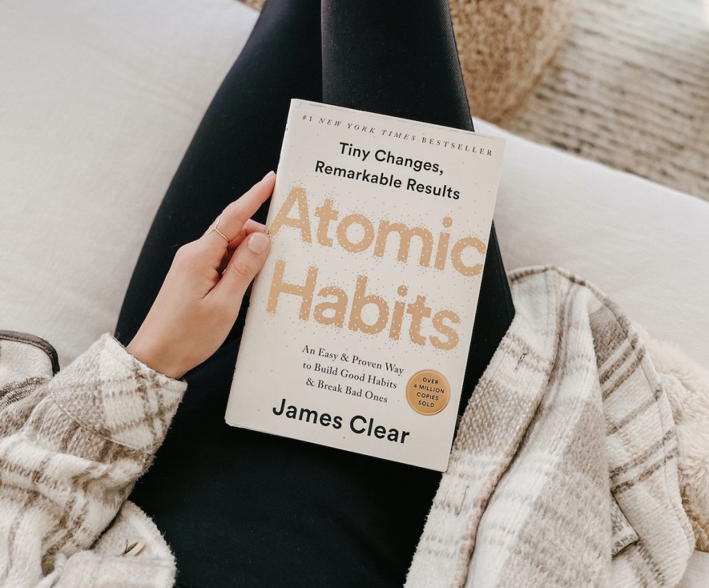 person sitting on couch holding atomic habits book in lap