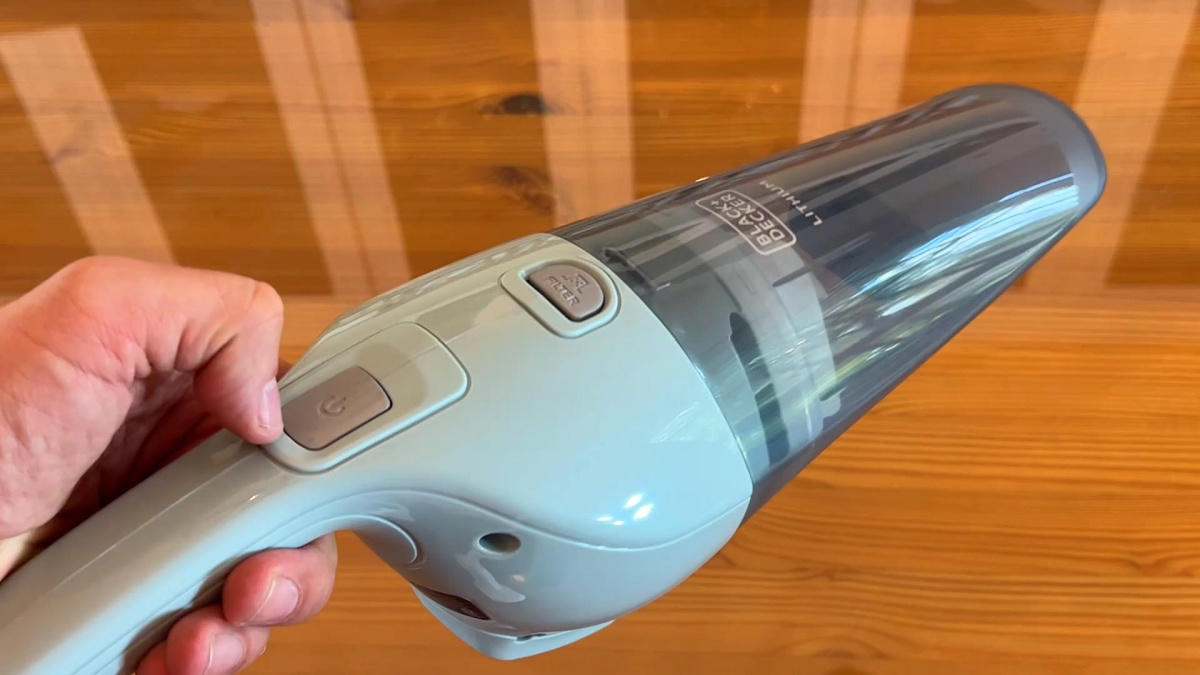 hand holding a cordless black and decker handheld vacuum near a floor